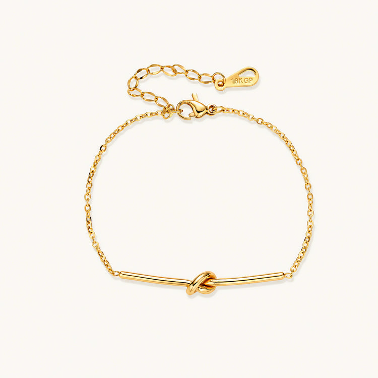 Delicate gold chain bracelet with minimalist bar and centered knot detail on cream background