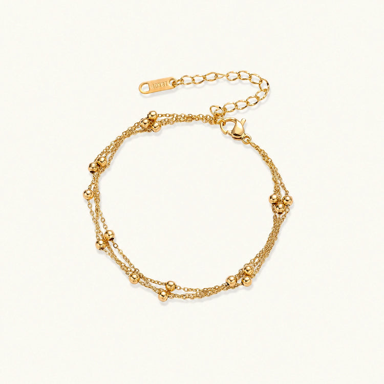 Three-strand gold-plated bracelet with clustered ball beads and adjustable clasp on cream background