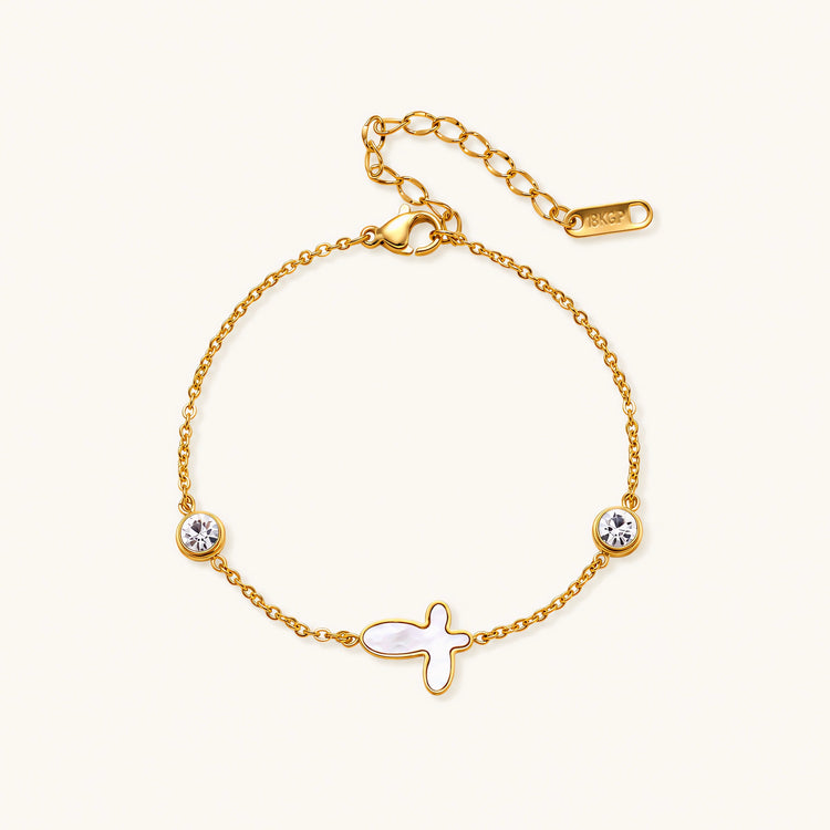 Gold chain bracelet with white mother of pearl butterfly pendant and two bezel-set crystals on cream background